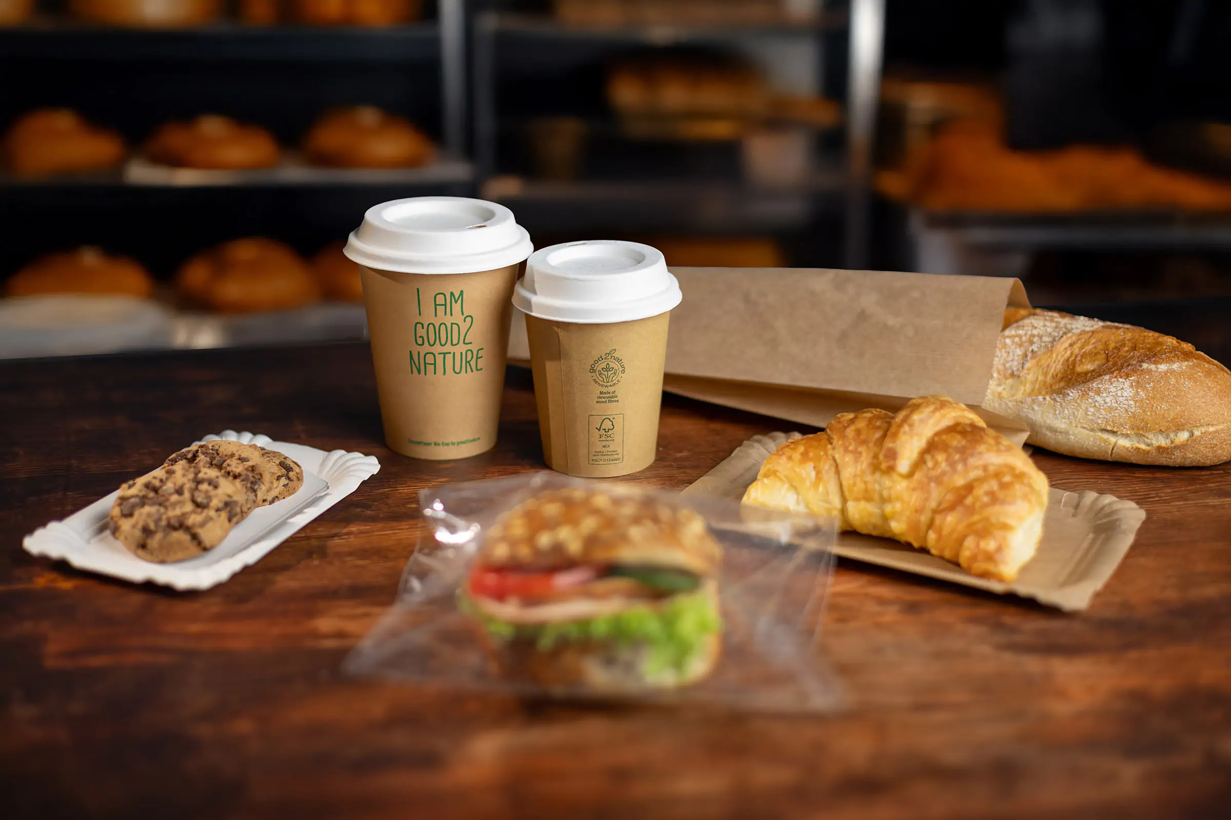 Verschiedene Bäckereiverpackungen und Kaffeebecher stehen auf einem Holztisch