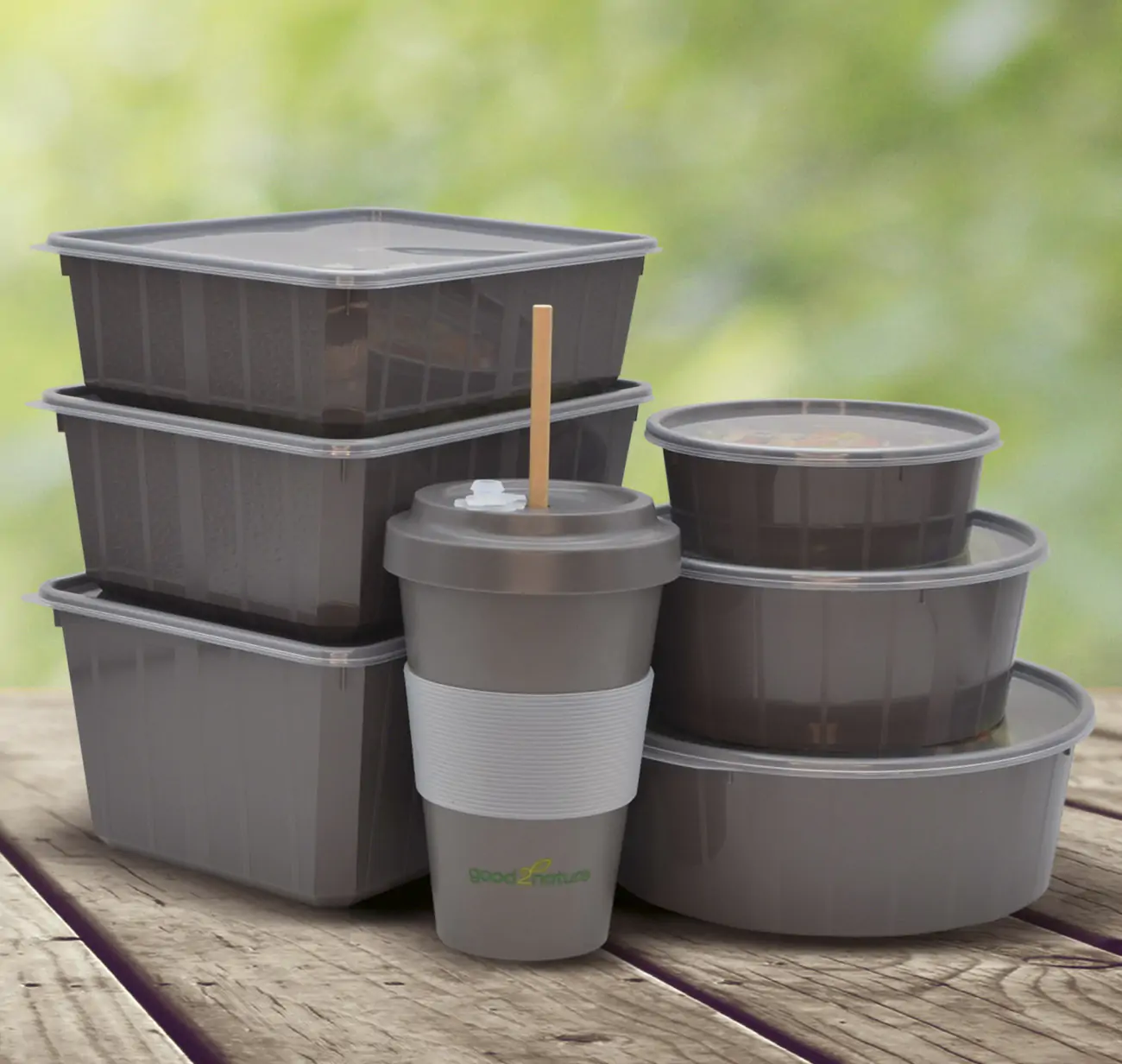 Mehrwegbecher und -boxen stehen auf einem Holztisch vor einem grünen Hintergrund