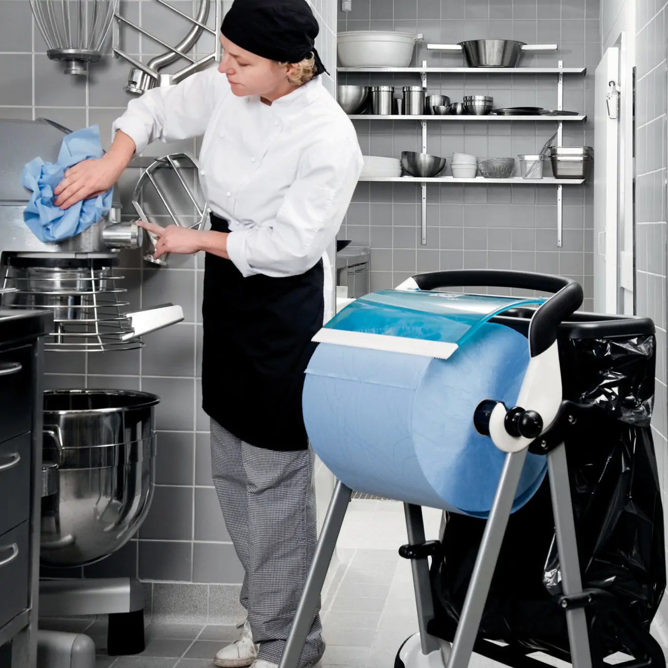 Eine Frau in einer Profiküche reinigt ein Gerät; neben ihr steht eine Rolle mit Einwegwischtüchern